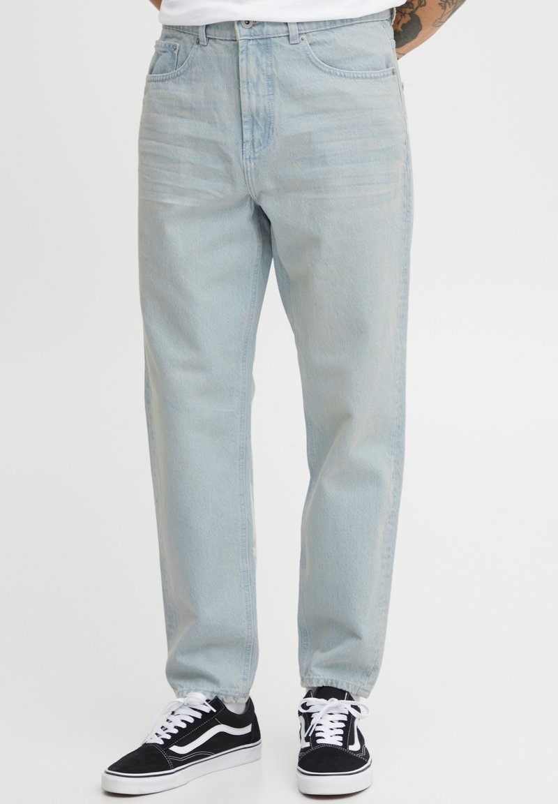 Vaqueros de denim azul claro con un diseño de pierna recta, estilo clásico de cinco bolsillos y un lavado desgastado. Llevados con zapatillas negras.
