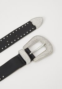 Cinturón de cuero negro con una hebilla incrustada de strass plateado, que presenta un extremo puntiagudo y múltiples agujeros a lo largo de la correa para su ajuste.