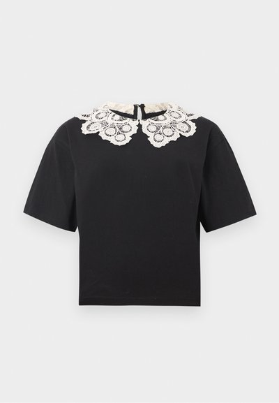 Haut court noir à manches courtes avec un large col en dentelle blanche présentant des motifs circulaires complexes et une fermeture éclair au dos.