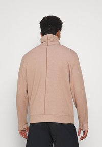 Suéter de color marrón claro con cuello alto, mangas largas y un detalle de costura central en la espalda. Fabricado en un tejido suave y texturizado.