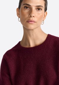 Burgundy knitted sweater with a wide neckline and ribbed accents. Soft texture and relaxed fit, featuring a classic, simple design.