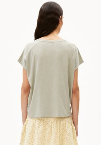 lichtgroene top met korte mouwen, een ontspannen, boxy fit en een zachte textuur, gecombineerd met een gestreepte gele rok met oogjes.