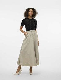 Svart stickad topp med texturerat mönster, kombinerad med en flödande beige kjol. Outfiten kompletteras av krämfärgade högklackade skor.
