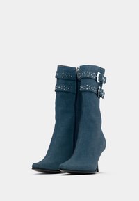Denim gležnjarji v temno modri barvi, z ostrim nosom, zoženim peto in dvema okrasnima trakovoma s srebrnimi zakovicami na vrhu.