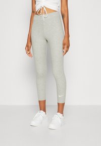 Leggings ajustados grises hechos de un material suave y elástico, con un logo de Nike en la parte inferior de la pierna izquierda y largo de tobillo recortado.