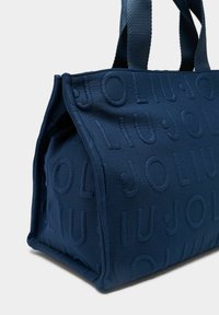 Tumesinist riidest kott reljeefse logoga, ruudukujuline, tugevate sangade ja tekstuurse pinnaga. Ideaalne igapäevaseks kasutamiseks.