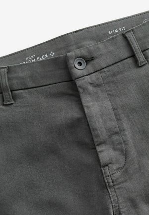 Pantalones de algodón de corte slim fit en gris oscuro con una textura suave, cuentan con cierre de botón y presillas para cinturón. Incluyen detalles de costura sutiles.