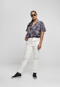Koszulka z krótkim rękawem w fioletowym tie-dye, zestawiona z białymi jeansami slim-fit i czarnymi sneakersami na wysokiej podeszwie. Uzupełniona okrągłymi okularami przeciwsłonecznymi.