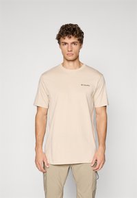 Beige bomull t-skjorte med korte ermer og rund hals, med en liten svart logo på venstre bryst. Glatt tekstur.