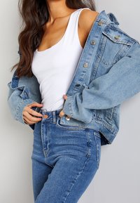 Vaaleansininen farkkutakki, väljää mallia suurilla napeilla, yhdistettynä valkoiseen toppiin ja korkeavyötäröisiin sinisiin farkkuihin.