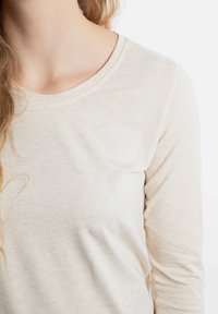 Beige langslank shirt met een ronde halslijn, gemaakt van zachte stof. Bevat een subtiele textuur en een soepele afwerking zonder zichtbare patronen.