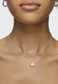 Collana in argento con un pendente bicolore a forma di trifoglio bianco e oro, appoggiato su una clavicola liscia e scoperta.