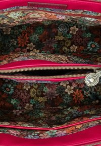 Interieur van een roze leren handtas met twee ritscompartimenten. Gevoerd met een bloemige stof in bruin, met kleurrijke bloemen en bladeren.