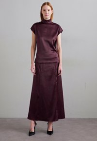 Burgundi satina topp kõrgema kraega, millele on kokku sobitatud pikad seelikud. Sile tekstuur, minimalistlik disain ja keha lähedane lõige. Mustad kõrged kontsad.