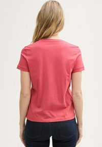 T-shirt corail à manches courtes en tissu doux, avec col rond et coupe décontractée. La vue de dos montre une texture lisse et sans motifs.