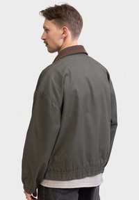 Olijfgroene bomberjack met een bruin corduroy kraag, elastische manchetten en tailleband. Soepele textuur met een comfortabele pasvorm.