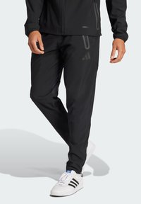 Pantalones deportivos negros con corte ajustado, que cuentan con cinturilla elástica, bolsillos con cremallera y detalles reflectantes. Combinados con zapatos blancos.