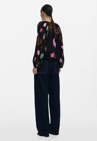 Svart blommig blus med rosa, gröna och vita mönster; långa, voluminösa ärmar; matchad med högmidjade mörkblå jeans.