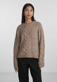 Chunky knit sweater in light brown, featuring cable patterns on the front and sleeves, with ribbed cuffs and hem, and a relaxed fit.