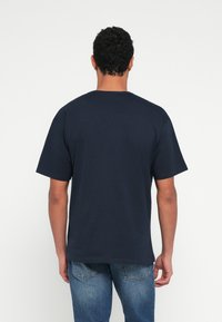 Μπλε ναυτικό βαμβακερό t-shirt με κοντά μανίκια, στρογγυλή λαιμόκοψη και χαλαρή εφαρμογή, εμφανίζεται από πίσω χωρίς ορατά λογότυπα ή σχέδια.