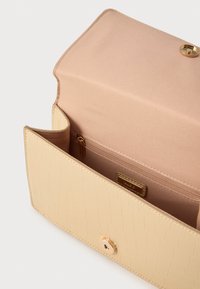 Torba iz umetnega usnja kremne barve s teksturo krokodilje kože in zlato pritisno zapiralo. Notranjost vključuje bež tkaninsko oblogo in žep z zadrgo.