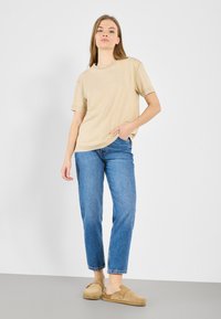Beige puuvillane t-särk lühikeste varrukatega, sobitatud helesiniste sirgete pükstega ja tan värvi libisevate kingadega; lihtne ja mugav disain.