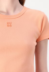 T-shirt à manches courtes côtelé pêche avec un col rond et le logo brodé "HUGO" de la même couleur sur la poitrine.
