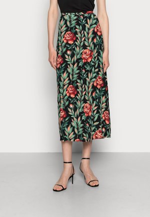 Jupe midi noire avec motif de roses rouges et feuilles vertes, portée avec des sandales noires à talons hauts et bretelles, et un haut noir.