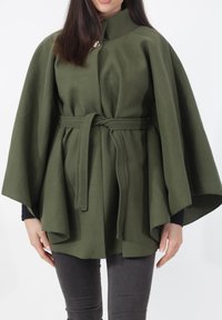 Olijfgroene wollen cape met een hoge kraag, vooraan sluiting met een knoop en een ceintuur in de taille. Heeft brede mouwen en een getextureerde afwerking.