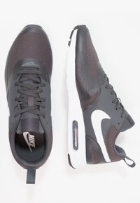 Gray Nike sneakers with a textured upper, white sole, and lace closure. Features a visible air cushion and logo detail on the side.