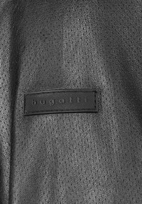 Cuero negro texturizado con pequeñas perforaciones, que presenta una etiqueta rectangular en relieve con "bugatti" en letras en relieve.