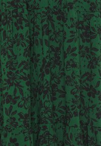 Tela verde con un patrón floral negro, que presenta pliegues y una superficie texturizada. El diseño consiste en varias formas de flores y hojas.