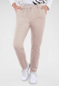 Svetloružové jogger nohavice vyrobené z mäkkej látky s elastickým pásom, bočnými vreckami a zúženými nohami, doplnené bielymi teniskami.