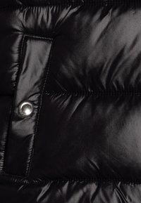 Juodas iki siūlų prisiūtas audinys su horizontaliu siuvimu pūstojo paltuko kišenėje, su sidabriniu snap mygtuko užsegimu.