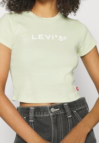 Lys grøn cropped t-shirt lavet af bomuld, med korte ærmer og et hvidt "LEVI'S" logo. Matchet med højtaljede shorts i mørk denim.
