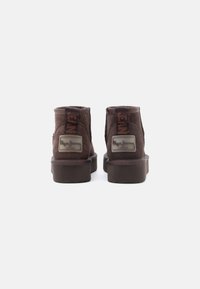 Pruun nahk-suede pahkluu saapad lapiku tallaga, bränditud sildid ja ümar varvaseloov. Silmapaistvad õmblemise detailid külgedel.