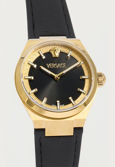 Montre-bracelet Versace ton or avec cadran noir, index horaires dorés, logo Méduse à 12 heures et bracelet en cuir noir affichant 10h09.