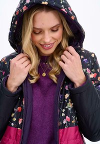 Květinová prošívaná bunda z tmavé látky s fialovou podšívkou a růžovými akcenty. Obsahuje kapuci a zipové zapínání, má jemnou texturu.
