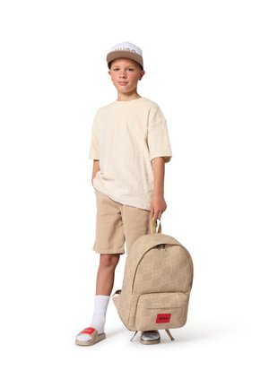 Sac à dos beige à motifs avec logo, haut à manches courtes texturé, short beige, chaussettes blanches et sandales slides avec accent rouge.