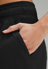 Musthave mustravi spordipüksid ribadega tekstuuriga, küljetasku ja elastse vöökohtaga. Käsi toetub tasku detailide jaoks.