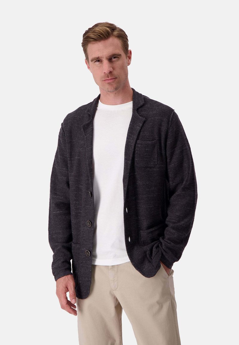 Cardigan grigio scuro realizzato in tessuto testurizzato, con colletto a rever, tre bottoni e due tasche frontali. Indossato sopra una maglietta bianca.