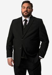 Completo tre pezzi nero con risvolto a punta, giacca monopetto e pantaloni coordinati. Camicia bianca e cravatta nera completano il look.