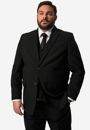 Schwarzer Dreiteiler mit abgesetztem Revers, einreihigem Blazer und passender Hose. Ein weißes Hemd und eine schwarze Krawatte runden den Look ab.