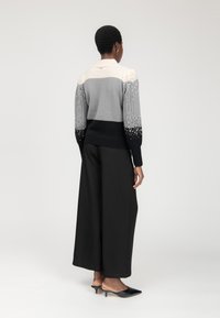 Maglione in maglia con sfumature di grigio, texture a treccia e dettagli di perline; abbinato a pantaloni neri a gamba larga e scarpe con tacco a kitten.