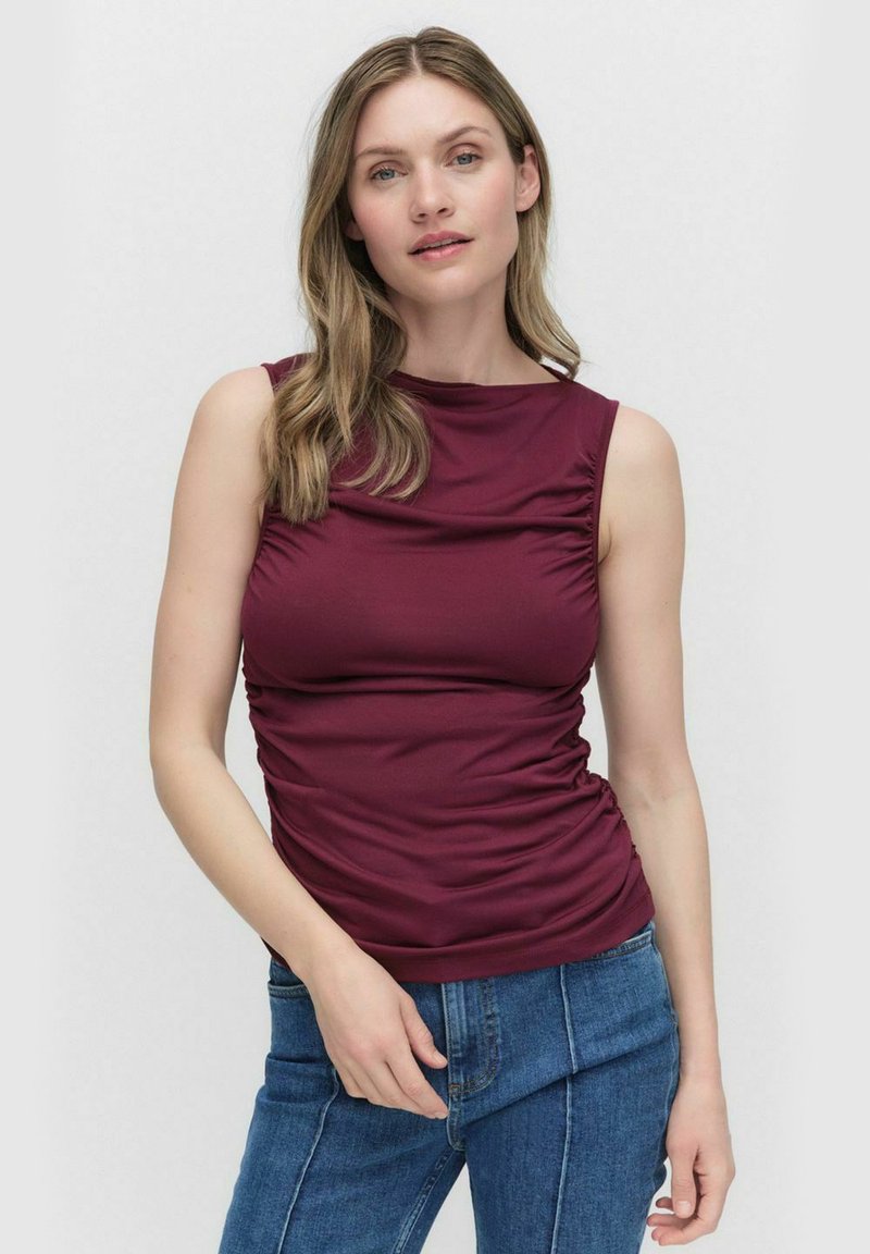 Bordeaux mouwloos shirt met gathered zijkanten, gemaakt van rekbare stof. Gladde textuur met een aansluitende silhoët en ronde halslijn.