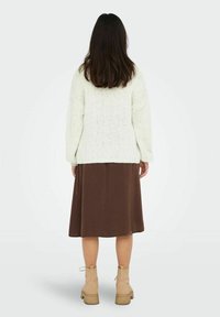 Pull en tricot crème avec des épaules tombantes, associé à une jupe midi marron et des bottines beiges. Le pull présente un motif en tricot texturé.