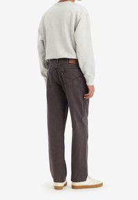 Sudadera gris con cuello redondeado combinada con jeans holgados de un gris oscuro, que cuentan con un parche de cuero en la parte trasera y dos bolsillos traseros. Zapatillas blancas.