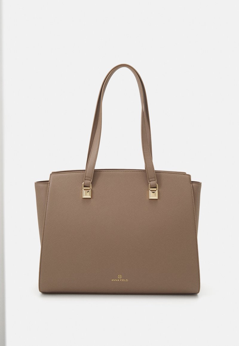 Brown faux leather tote bag with two straps, gold square hardware accents, and a smooth texture; features a minimalist logo at the base.