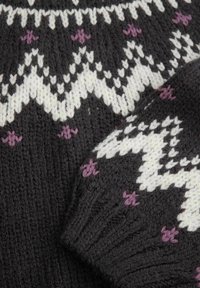 Ciemna dziana tkanina z białymi wzorami w zygzak oraz małymi fioletowymi akcentami w kształcie krzyża, ukazująca mankiet rękawa i część ciała.