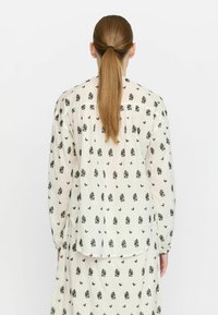 Blusa leggera color crema con stampa floreale nera. Maniche lunghe, vestibilità comoda e orlo leggermente curvato sul retro.